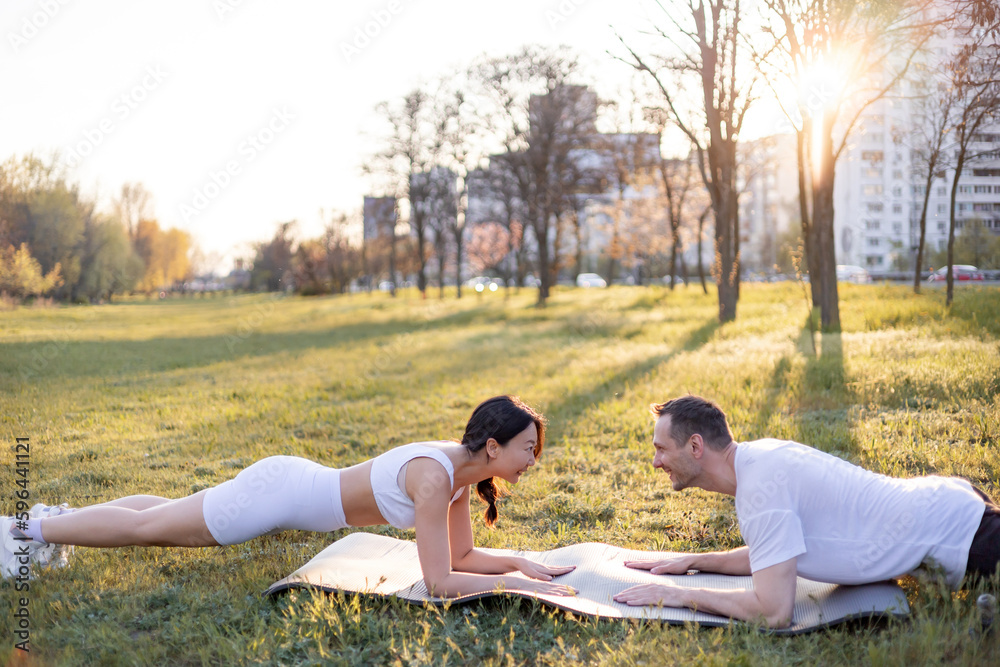 Asian famale and caucasian male couple Exercise in the outdoor park in the morning. They are healthy, smiling and happy. fitness concept, health care.