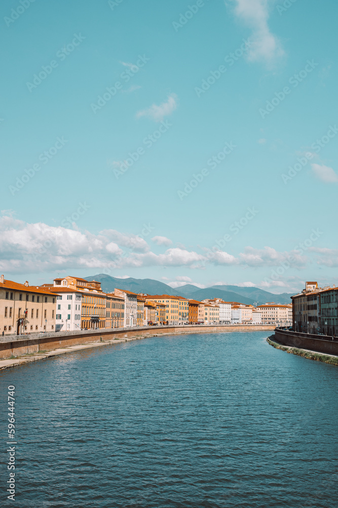 Beautiful view of buildings along the Arno river in Pisa, Italy. A bridge passes over the river and houses on both sides are overlooking the water. High quality photo