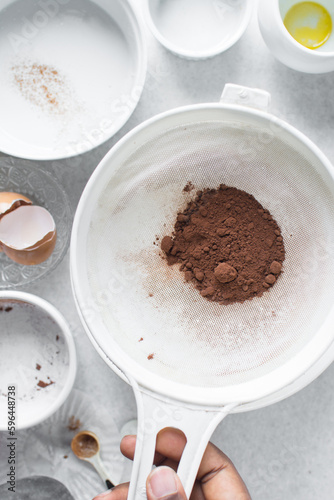 Cocoa powder in a white sieve  sifting cocoa powder into a large bowl