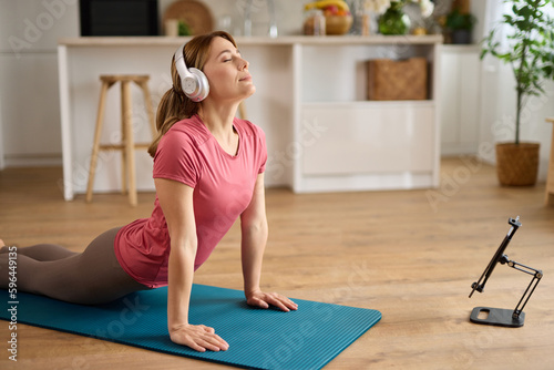Young woman with headphones practicing yoga at home while watching tutorial lessons on digital tablet