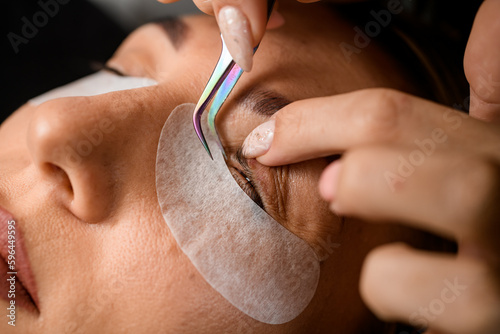 close-up of the female eyelid and eyelashes that beautician corrects with tweezers. Eyelash extension.