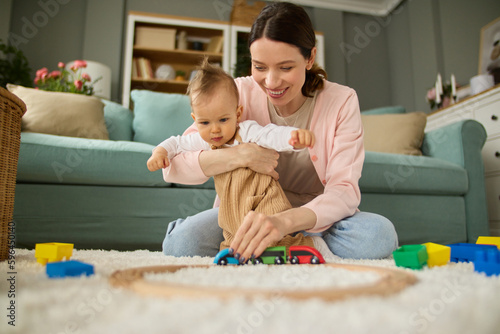 Joyful mother and baby boy playing with toys on a carpet at home