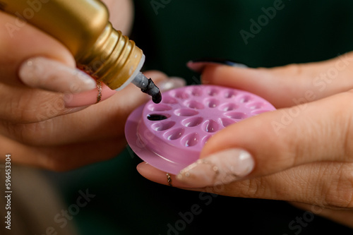 Selective focus on palette with black glue for eyelash extensions in female hands. photo