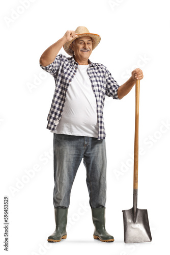 Full length portrait of a happy mature farmer with a shovel greeting with hat Fototapet