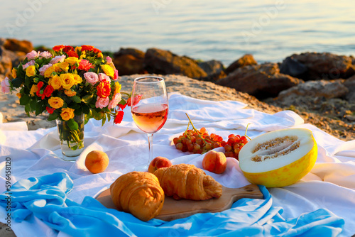 Picnic at sunrise. A glass of wine and flowers stand on a blanket overlooking the sea