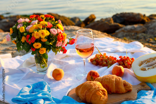 Picnic at sunrise. A glass of wine and flowers stand on a blanket overlooking the sea