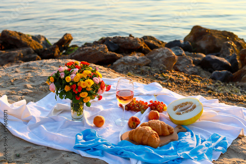 Picnic at sunrise. A glass of wine and flowers stand on a blanket overlooking the sea