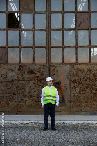 Caucasian male builder in hardhat standing near wall of unfinished building. Competent architect examining and controlling working process at construction site. © sakoqwakestock