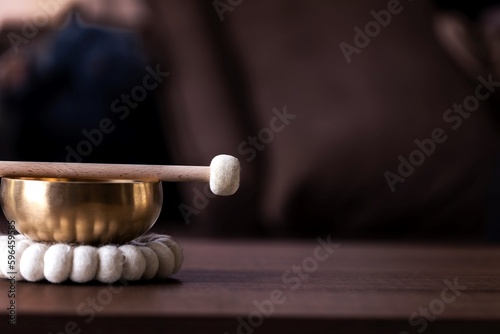 A close up of half of a tibetan singing bowl with a mallet on it and some negative space to the right. The himalayan bowl is used for stress relief, relaxation and meditation.