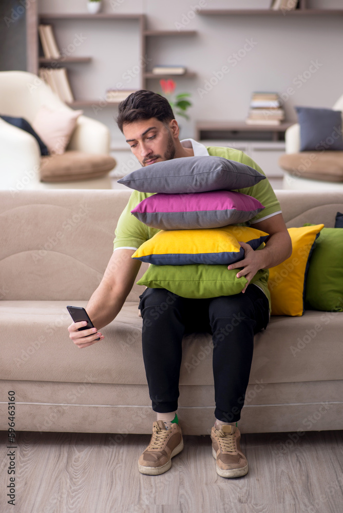 Obraz premium Young man with a lot of pillows sitting on the sofa