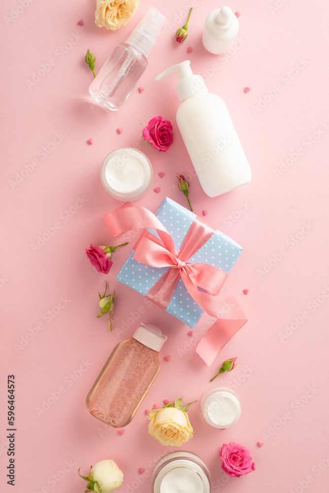 Soft floral beauty concept. Top view flat lay of pump bottle, pipette, cream bottles and tubes with flowers present box on pastel pink background