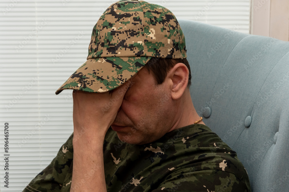 An elderly military man of 45-50 years covered his face with his hands while sitting in a chair. Concept: mental disorders in military personnel, treatment by a psychotherapist.