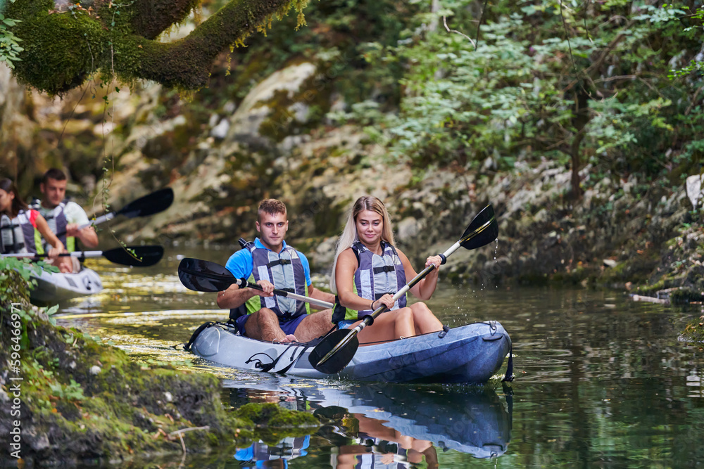 A young couple enjoying an idyllic kayak ride in the middle of a beautiful river surrounded by forest greenery A young couple enjoying an idyllic kayak ride in the middle of a beautiful river surrounded by forest greenery