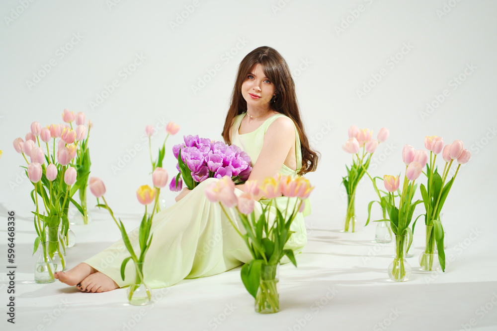 a woman in a delicate dress sits on the floor with bouquet surrounded by tulips 