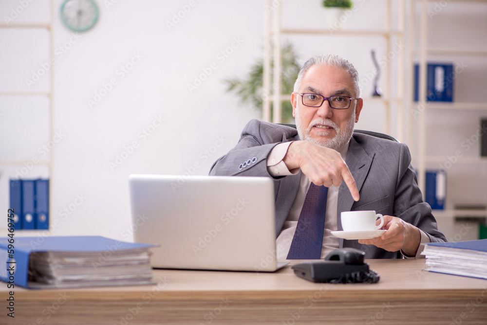 Old male employee drinking coffee in the office