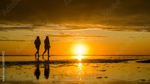 two women walking along the seashore in the golden hour of sunset on a summer afternoon at the beach
