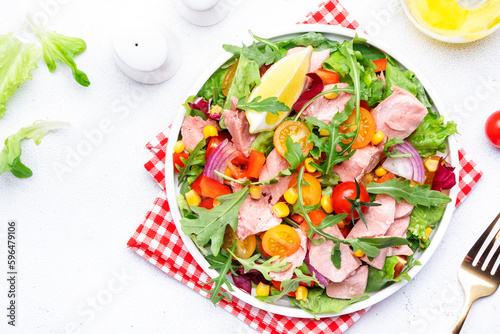 Canned Tuna salad with colorful cherry tomatoes, red onion, sweet corn, paprika, lettuce, radicchio and arugula. White table background, top view