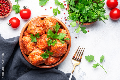 Pork and beef meatballs in tomato sauce in wooden bowl on white table background, spices and herbs. Delicious home cooking. Top view