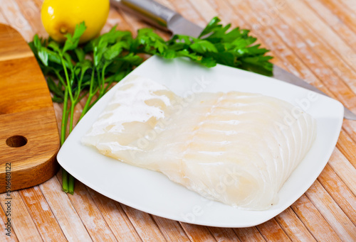 Fresh raw kingklip fillet with greens, lemon and spices on wooden background. Cooking ingredients photo