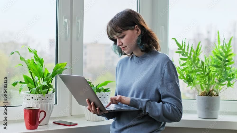 Young female uses a laptop at home near the window