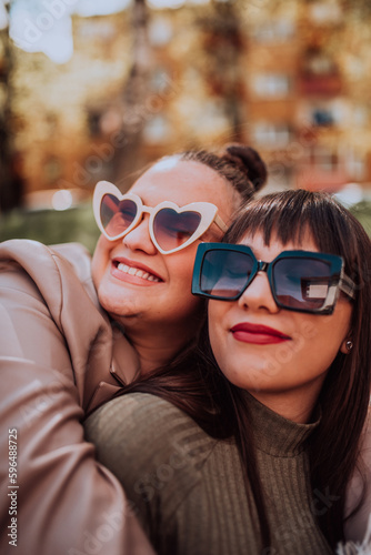 Two young women embrace each other emotionally outside on a sunny day while wearing sunglasses