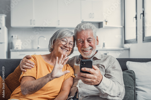 Happy retired family couple using mobile phone for video call together, talking to relations, getting good news, having fun, smiling and laughing. Carefree mature pensioners chatting online on cell.