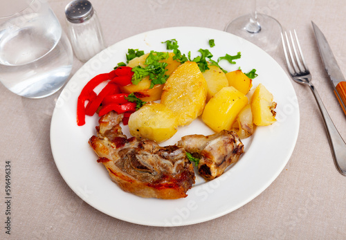 Appetizing side dish of baked lamb leg with potatoes and red pepper, decorated with fresh chopped herbs