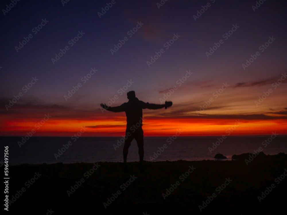man opening his arms at the edge of the cliff at sunset, contemplating the beauty of the landscape