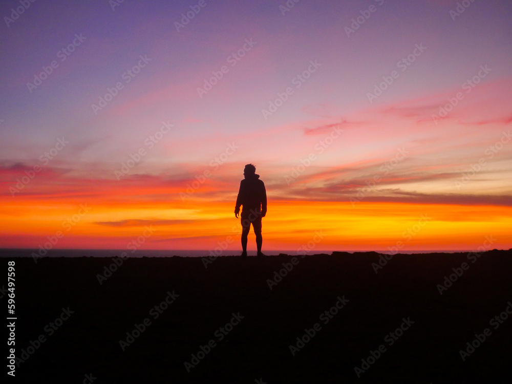 Silhouette of middle-aged man on cliff edge at sunset