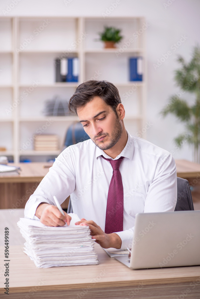 Young male employee and too much work at workplace