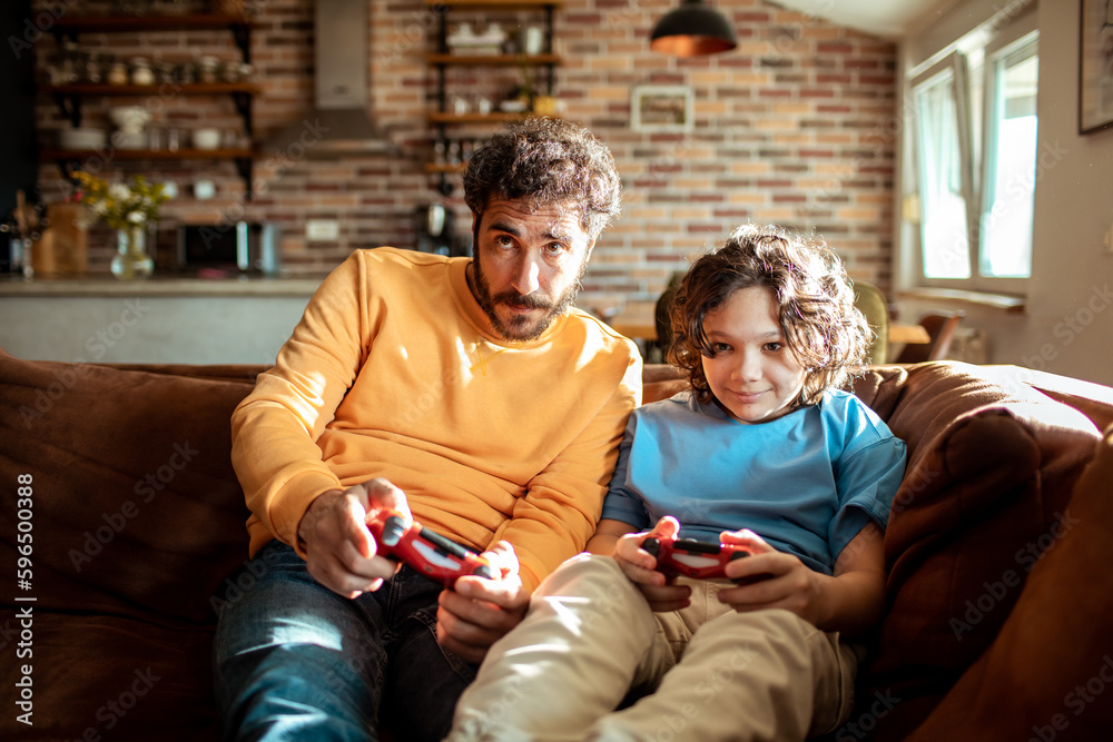 Father and son playing videos games on a gaming console in the living room of their home