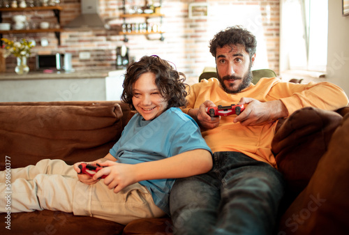 Father and son playing videos games on a gaming console in the living room of their home