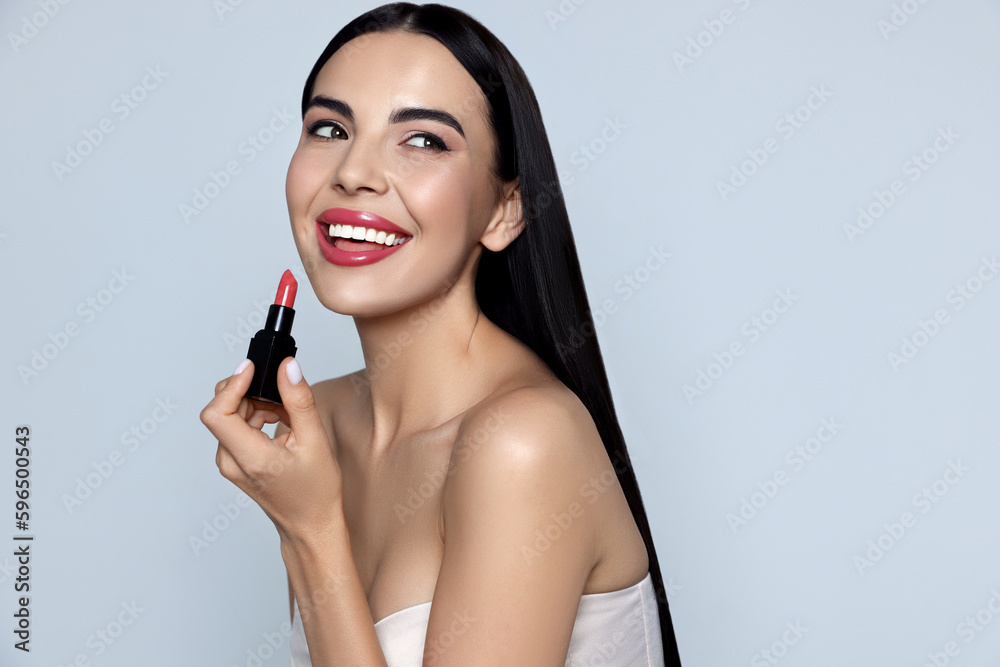 Young woman with beautiful makeup holding glossy lipstick on light gray background Young woman with beautiful makeup holding glossy lipstick on light gray background