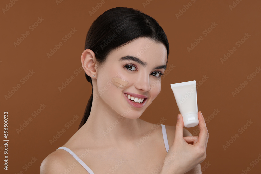 Teenage girl holding tube with foundation on brown background Teenage girl holding tube with foundation on brown background