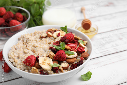 Fototapeta Naklejka Na Ścianę i Meble -  Delicious oatmeal with freeze dried berries, banana, nuts and mint on white wooden table, closeup