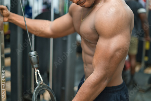 A young African man is determinedly weight training in a gym, demonstrating their energetic physical fitness and muscular build.