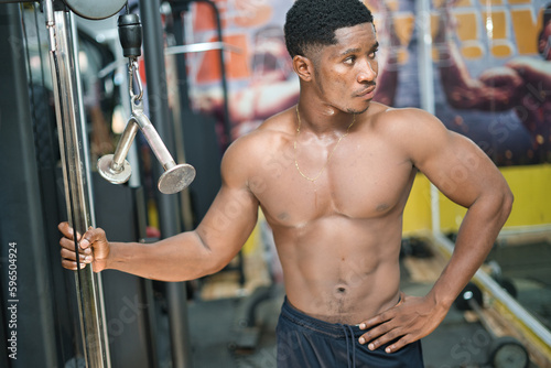 An African young male is weight training in a gym, building strength and physical fitness to achieve their desired muscular build. © Ibrahim