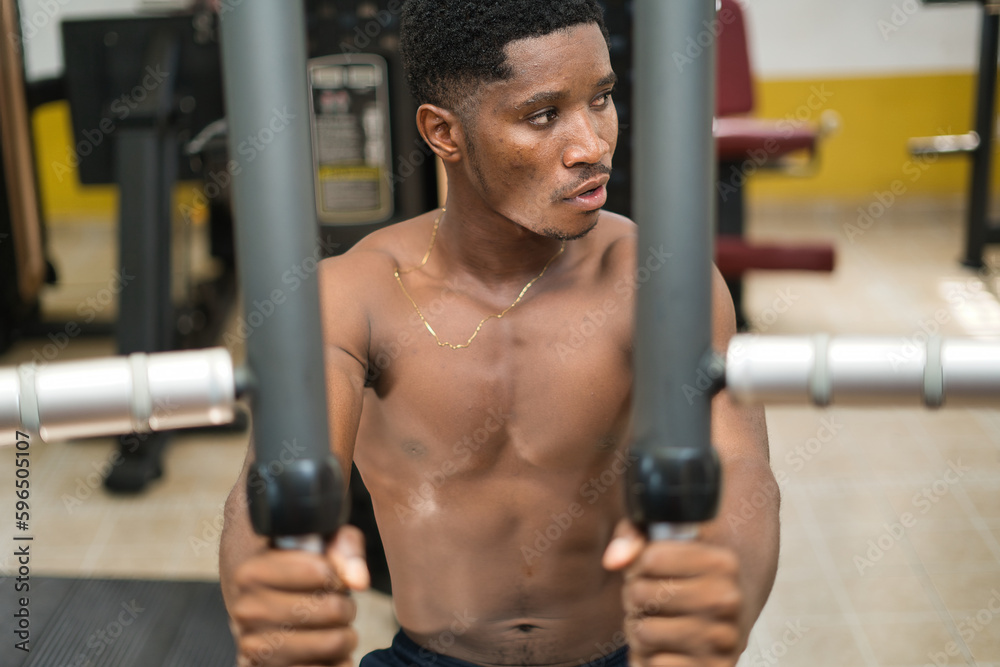 A young African male in a gym, exercising for physical fitness and well-being with weight training to build their muscular strength. A young African male in a gym, exercising for physical fitness and well-being with weight training to build their muscular strength.