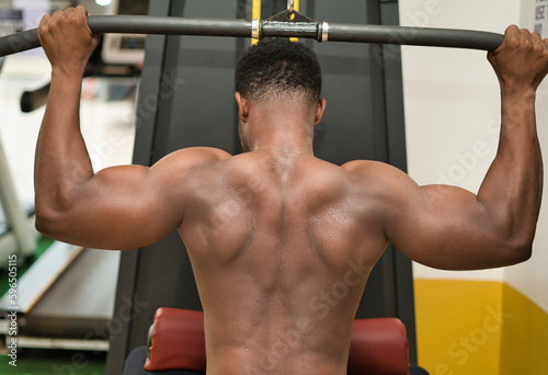 A muscular black male weight training in a gym, building their muscular strength and vitality through physical fitness.