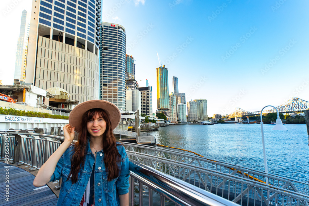 portrait of a beautiful girl standing on the city reach boardwalk in brisbane cbd with large skyscrapers in the background; brisbane skyline byt the river, australia