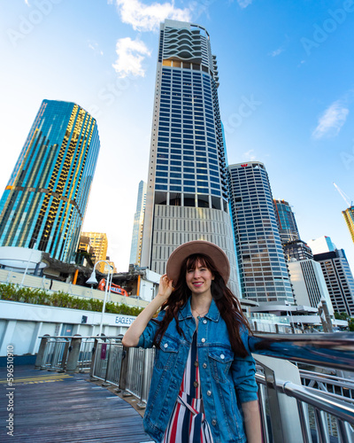 portrait of a beautiful girl standing on the city reach boardwalk in brisbane cbd with large skyscrapers in the background  brisbane skyline byt the river, australia © Jakub