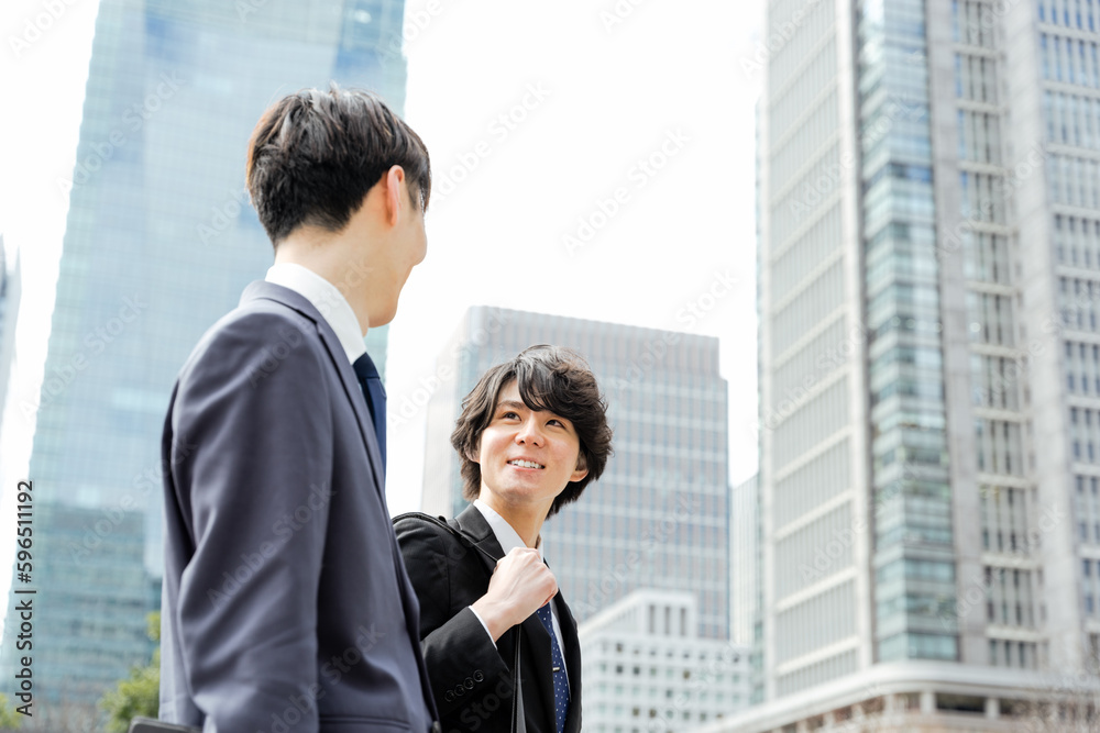 オフィス街で会話しながら歩く20代から30代のビジネス中の2人のスーツの男性 オフィス街で会話しながら歩く20代から30代のビジネス中の2人のスーツの男性