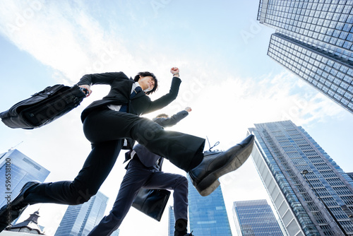青空の高層ビルに囲まれた都会を勢いよく走りだす2人のスーツのビジネスマンの男性