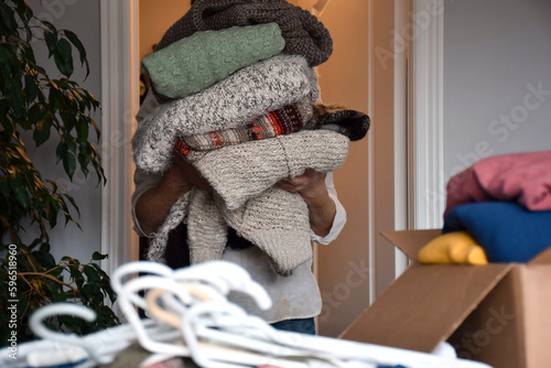 Принти на полотні Woman holding a huge stack of winter knit sweaters, organizing and sorting cloth