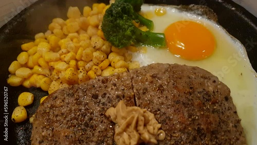 Japanese style hamburge steak serve in steaming hot plate with egg corn and mustard clsoe-up shot photo