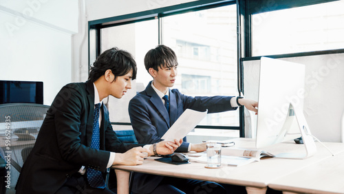 オフィスでパソコンへの入力内容を確認する若い2人のビジネスマンの男性 photo