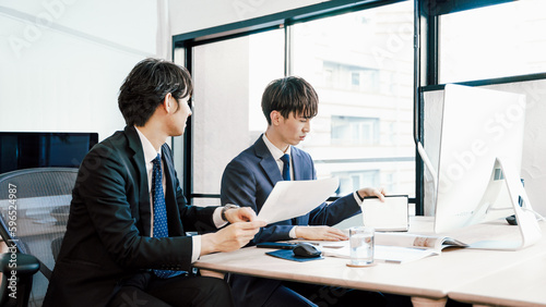 オフィスでパソコンを前に協力してデスクワークをする若い2人のビジネスマンの男性 photo