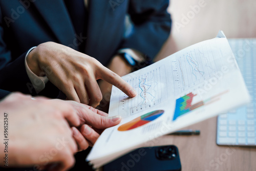 男性2人でグラフやデータの書かれた紙の資料の書類に指差しするボディパーツの手元 photo