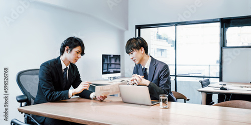 中小企業のオフィスの会議テーブルで打ち合わせをするビジネスマンの男性社員とインターンシップの男性 photo