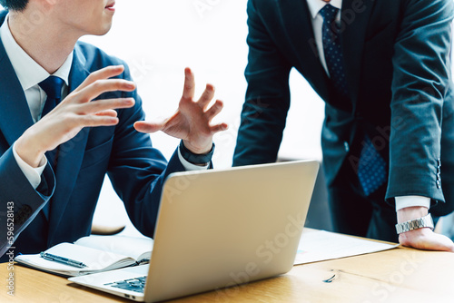 スーツを着た2人のビジネスパーソンの男性の机のノートパソコンの前での会議と相談と説明の手元のシーン